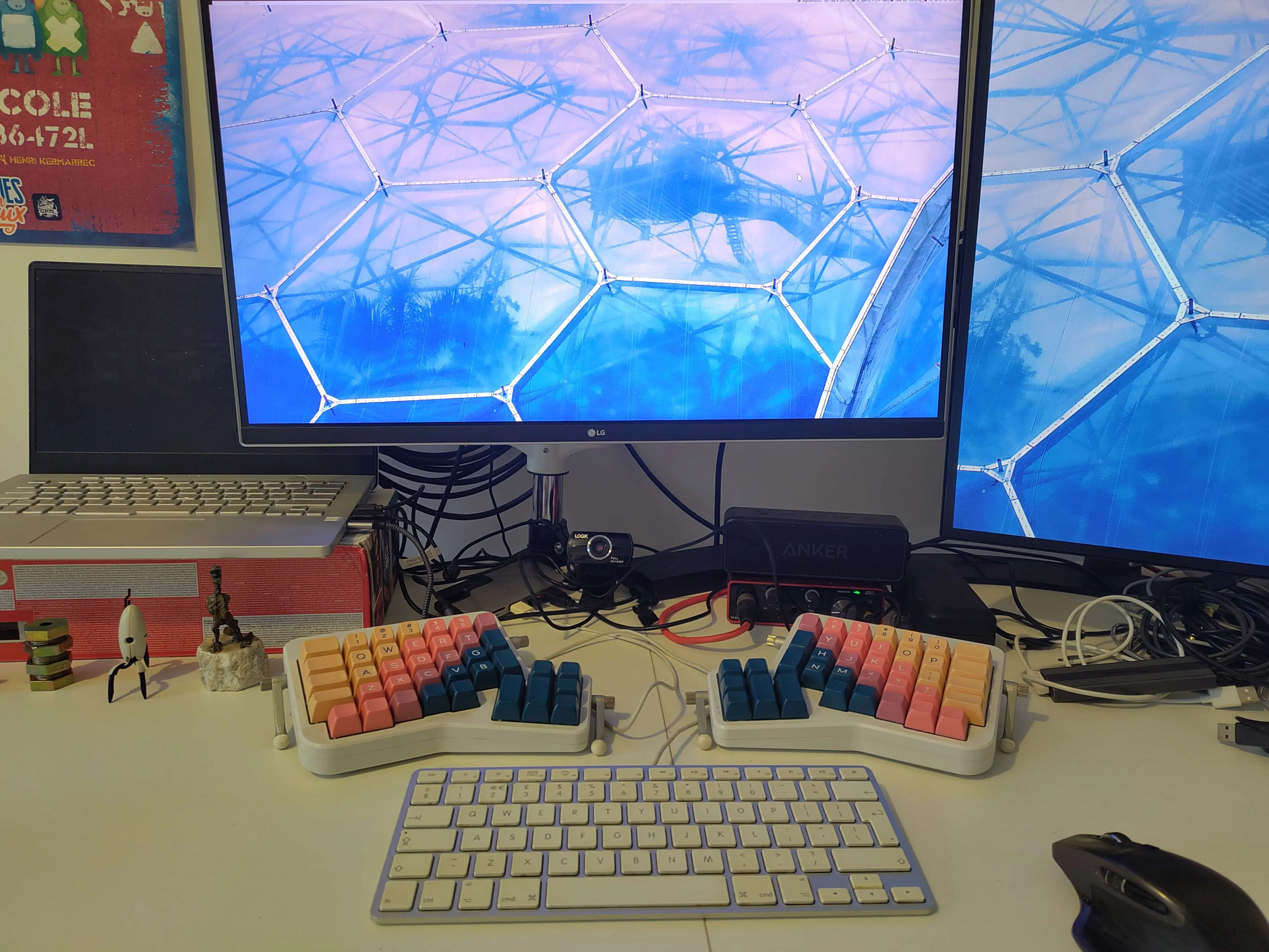 Picture of a desktop setup with two screens and two keyboards: a low profile Apple keyboard below two halves of a colourful maximalist split keyboard.